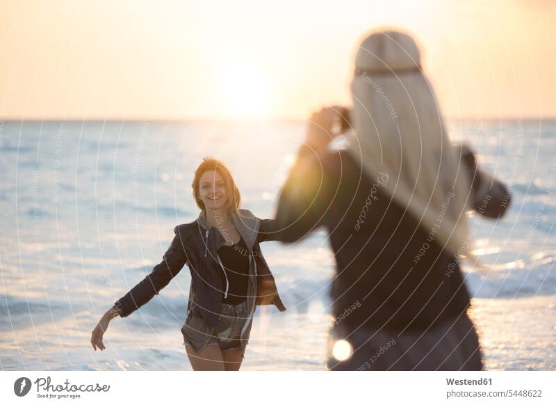 Friends taking pictures on the beach at sunset romantic lyrical Romance beaches vacation Holidays dancing dance happiness happy Sea ocean Travel water sunshine