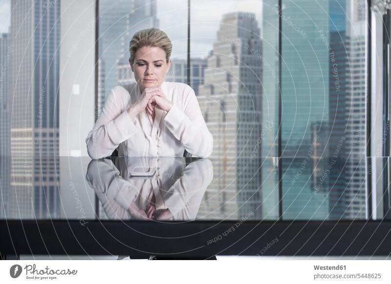 Serious businesswoman sitting at desk in city office looking at cell phone businesswomen business woman business women offices office room office rooms