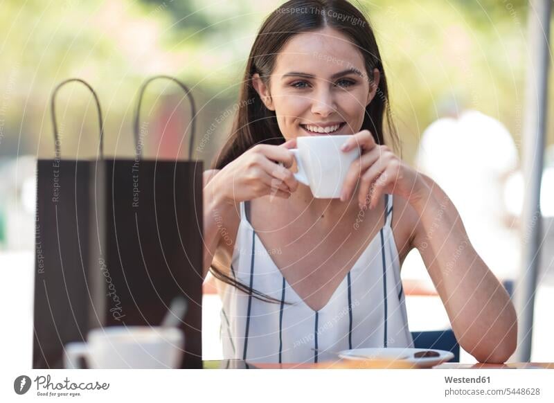 Smiling woman with shopping bag enjoying coffee at cafe happiness happy smiling smile shopping-bag shopping-bags shopping bags females women buying Adults