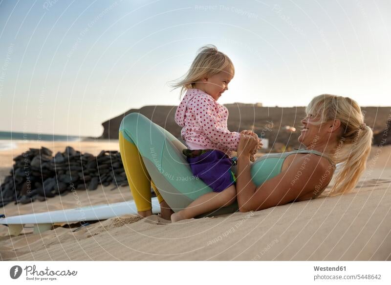 Spain, Fuerteventura, happy mother and daughter on the beach next to surfboard at sunset beaches daughters mommy mothers ma mummy mama surfboards Fun having fun