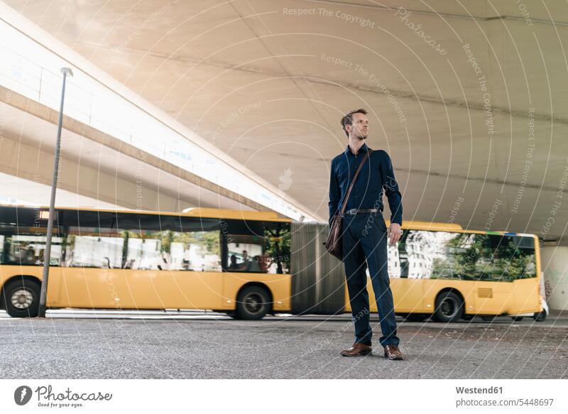 Businessman standing at underpass with bus in background Business man Businessmen Business men busses business people businesspeople business world
