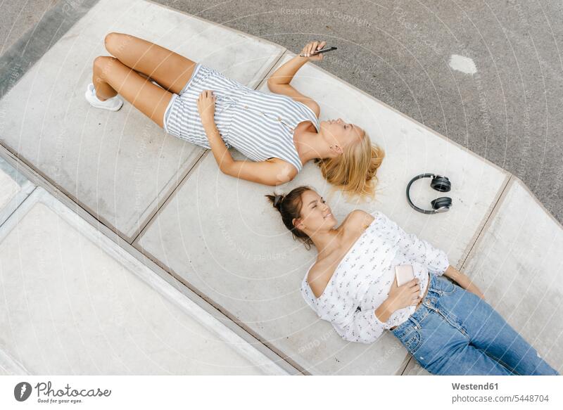 Two young women with cell phone and headphones in a skatepark female friends headset mobile phone mobiles mobile phones Cellphone cell phones parks