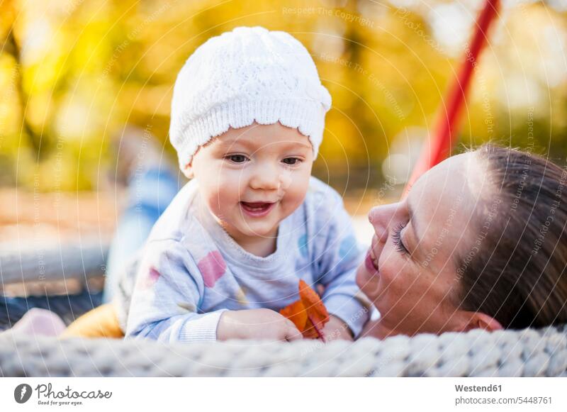 Portrait of happy baby girl relaxing with her mother on a swing in autumn fall playground play yard play ground playgrounds mommy mothers ma mummy mama