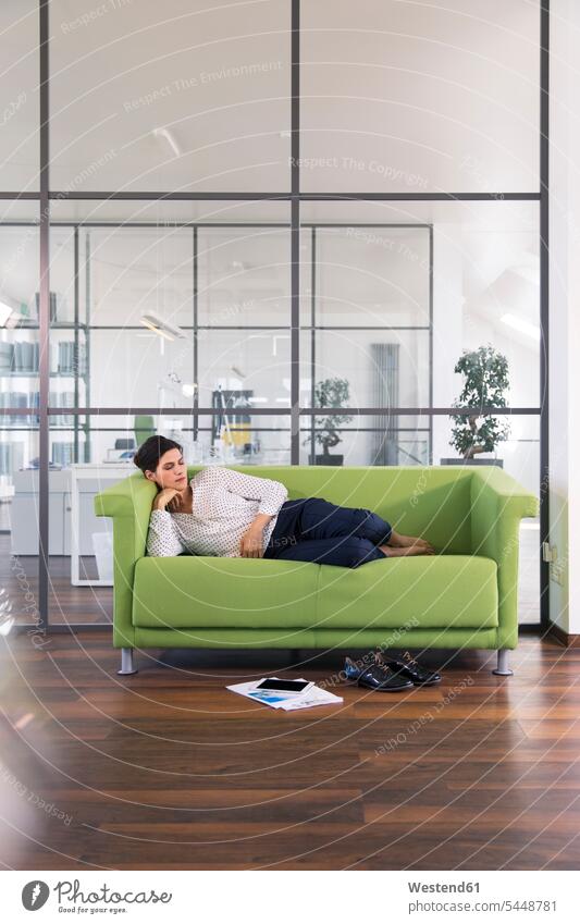 Businesswoman taking a nap lying on a couch in the office caucasian caucasian ethnicity caucasian appearance european cozy sociable comfortable cosy resting