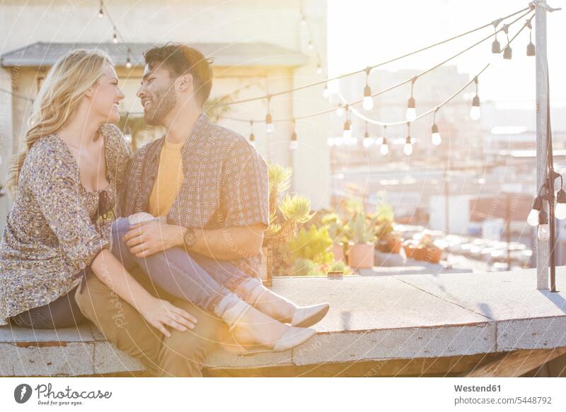 Happy couple sitting on rooftop, embracing each other in love roof terrace deck embrace Embracement hug hugging Seated happiness happy twosomes partnership