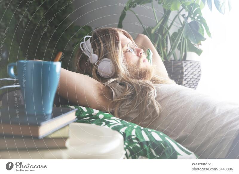 Man with long hair and beard lying on sofa listening music with headphones man men males Adults grown-ups grownups adult people persons human being humans
