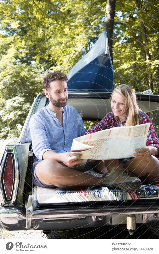 Smiling young couple with map and canoe in car at a brook smiling smile twosomes partnership couples automobile Auto cars motorcars Automobiles forest woods