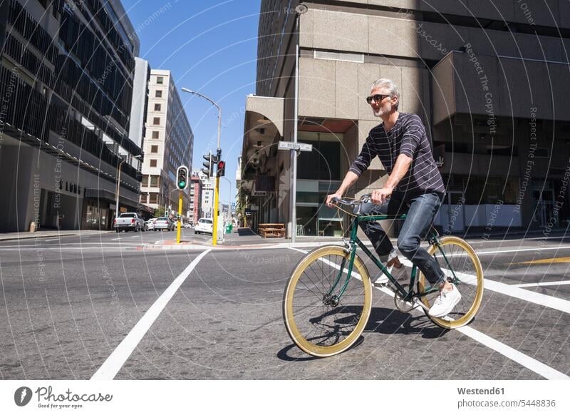 Mature man riding bicycle in the city bikes bicycles riding bike bike riding cycling bicycling pedaling on the move on the way on the go on the road town cities