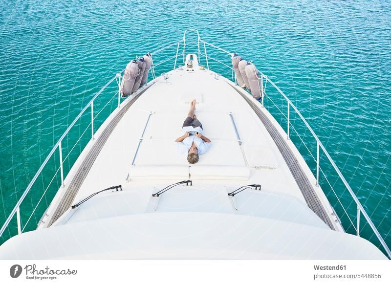 Smiling man lying on deck of his motor yacht using tablet men males motor yachts Adults grown-ups grownups adult people persons human being humans human beings