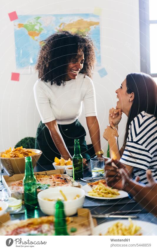 Two happy young women at dining table Pizza Pizzas friends laughing Laughter Table Tables eating Beer Beers Ale Food foods food and drink Nutrition Alimentation
