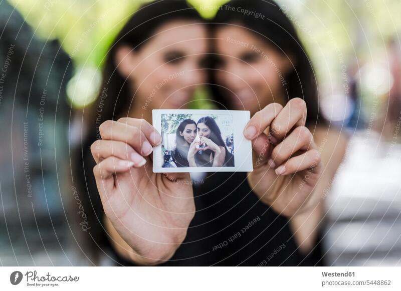 Two twin sisters holding an instant photo of themselves photograph photographs photos female friends image images picture pictures siblings brother and sister