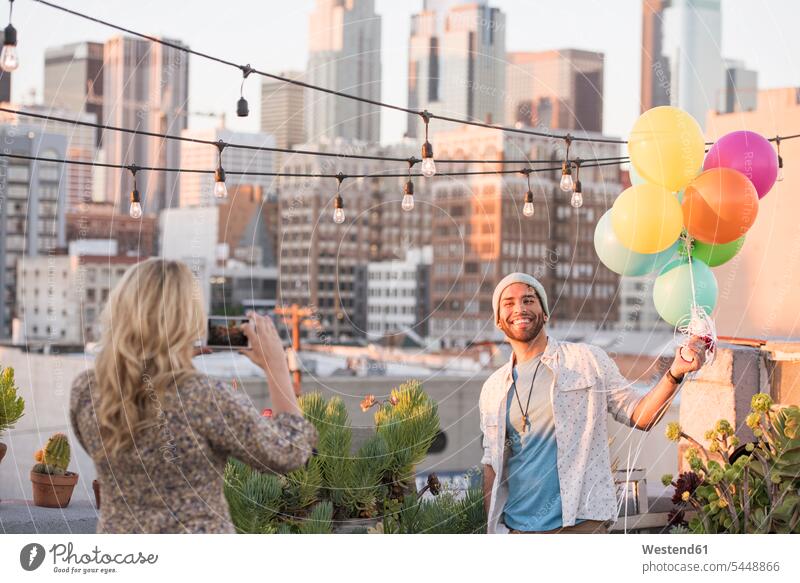 Young couple with balloons standing on rooftop terrace, using smart phone happiness happy Smartphone iPhone Smartphones roof terrace deck photographing twosomes