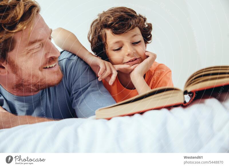 Father and son reading book in bed books lying laying down lie lying down father pa fathers daddy dads papa relaxed relaxation sons manchild manchildren beds