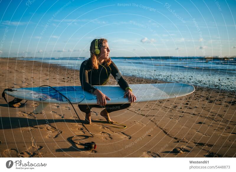 Young woman with surfboard listening music on the beach by sunset surfboards surfer female surfer surfers female surfers headphones headset surfing surf ride