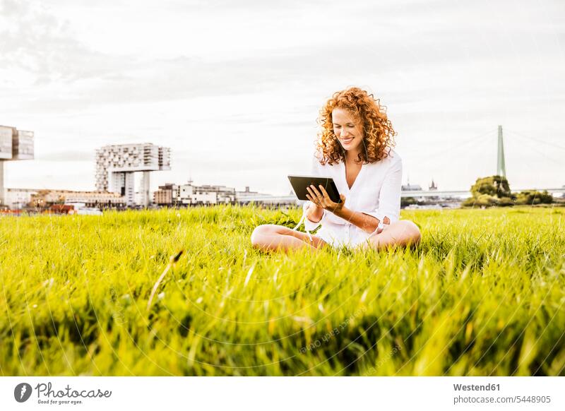 Germany, Cologne, young woman sitting on meadow looking at tablet meadows females women digitizer Tablet Computer Tablet PC Tablet Computers iPad Digital Tablet