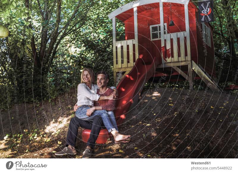 Happy couple sitting on slide of garden shed in the woods Seated Chute playground slide slides Chutes twosomes partnership couples smiling smile forest forests
