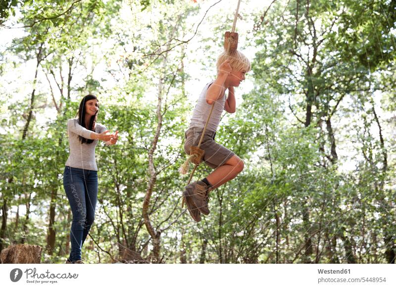 Mother with son on swing in forest mother mommy mothers ma mummy mama swing set playground swing swingset sons manchild manchildren boy boys males woods forests