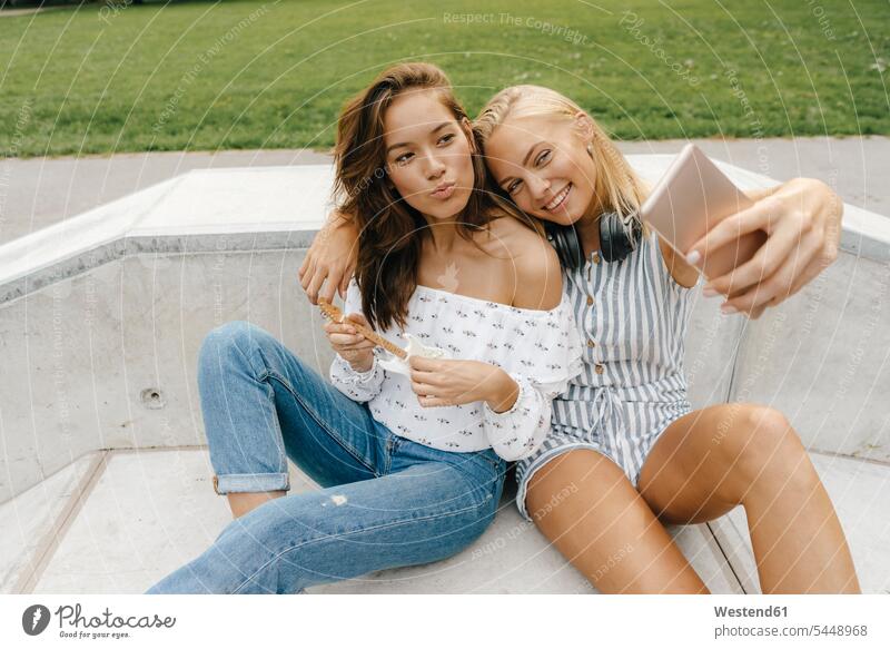Two happy young women taking a selfie in a skatepark female friends Skateboard Park skate park happiness Selfie Selfies woman females mobile phone mobiles