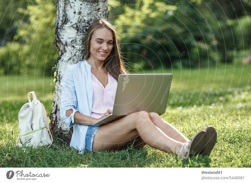Smiling young woman using laptop on a meadow smiling smile park parks females women Laptop Computers laptops notebook Adults grown-ups grownups adult people