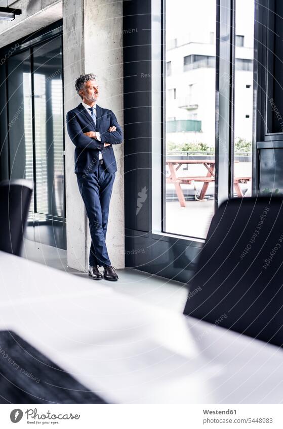 Mature businessman standing in office loooking out of window Businessman Business man Businessmen Business men looking view seeing viewing offices office room