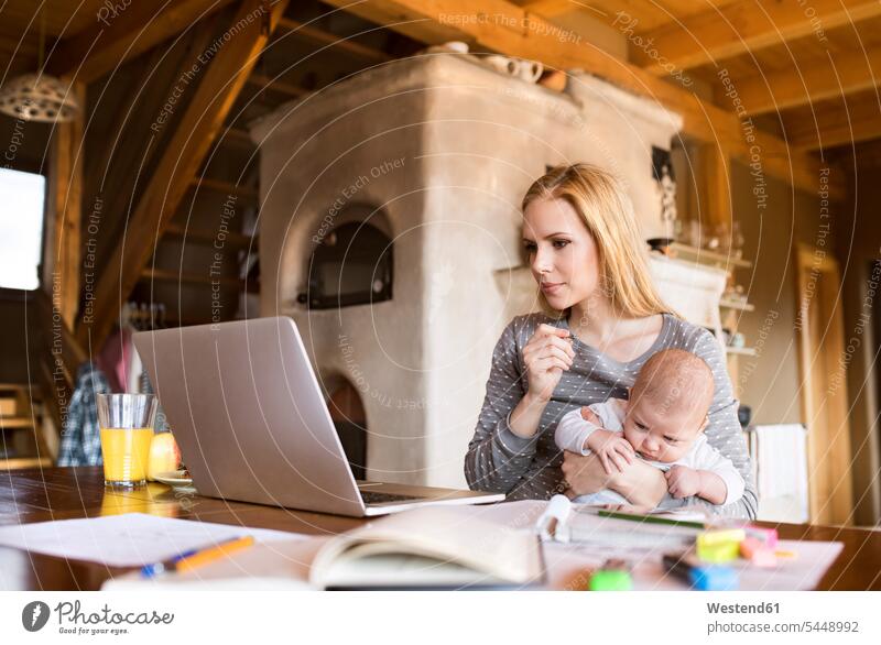 Mother with baby at home using laptop infants nurselings babies mother mommy mothers ma mummy mama Laptop Computers laptops notebook people persons human being