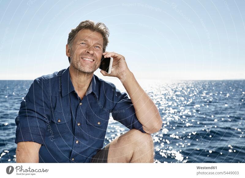 Portrait of smiling mature man on the phone in front of the sea men males call telephoning On The Telephone calling portrait portraits Adults grown-ups grownups