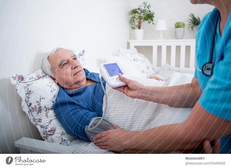 Gereatric nurse measuring blood pressure of patient, lying in bed assistance Looking After support care elderly care geriatric care laying down lie lying down