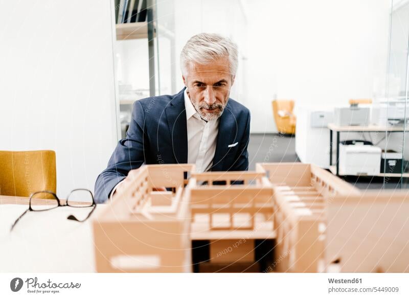 Mature businessman examining architectural model in office offices office room office rooms architects scrutiny scrutinizing Businessman Business man