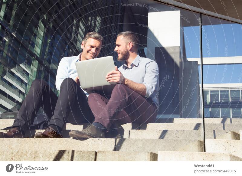 Two smiling businessmen sitting on stairs using laptop smile Laptop Computers laptops notebook stairway Seated Businessman Business man Businessmen Business men