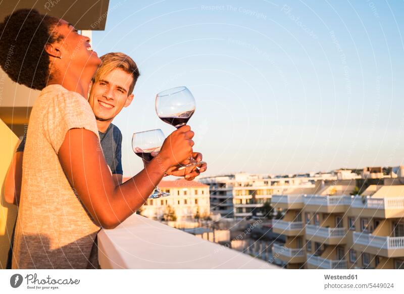 Happy young couple drinking wine on balcony balconies Wine Glass Wine Glasses Wineglass Wineglasses twosomes partnership couples relaxed relaxation