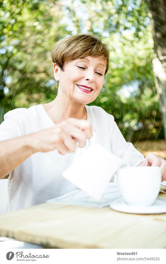 Smiling senior woman pouring milk into cup of coffee outdoors smiling smile females women Coffee senior women elder women elder woman old Adults grown-ups