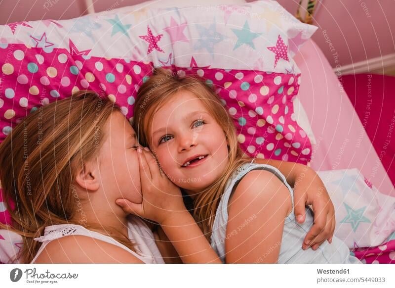 Girl lying on bed with her little sister telling a secret sisters girl females girls beds portrait portraits siblings brother and sister brothers and sisters