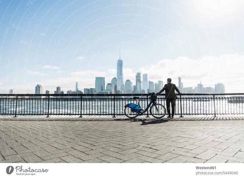 USA, man with bicycle at New Jersey waterfront with view to Manhattan bikes bicycles New York State men males Businessman Business man Businessmen Business men