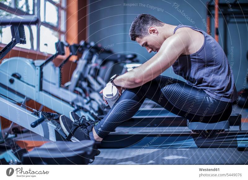 Young man having a break at rowing machine in gym exercising exercise training practising gyms Health Club men males fitness sport sports Adults grown-ups