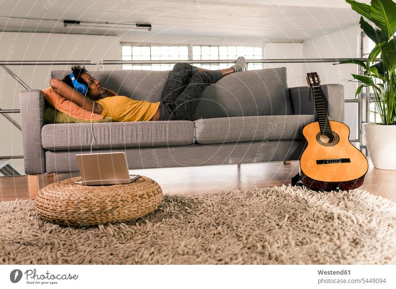 Young woman lying on couch with headphones connected to laptop settee sofa sofas couches settees headset Laptop Computers laptops notebook laying down lie