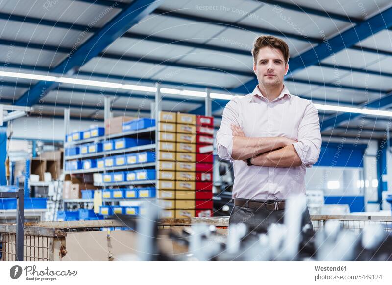 Employee standing in shop floor with arms crossed, portrait factory employee clerk employees clerks expert professional young man young men portraits working