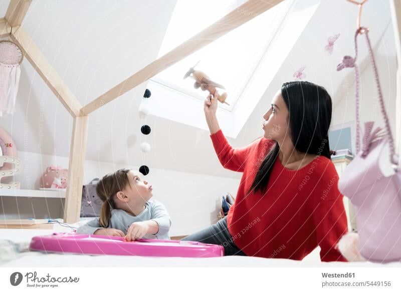 Mother and toddler daughter playing with toy plane in nursery mother mommy mothers ma mummy mama daughters children's room Kids Room child's room parents family