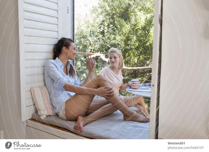 Two smiling young women separated by windowpane female friends woman females relaxed relaxation smile sitting Seated mate friendship Adults grown-ups grownups