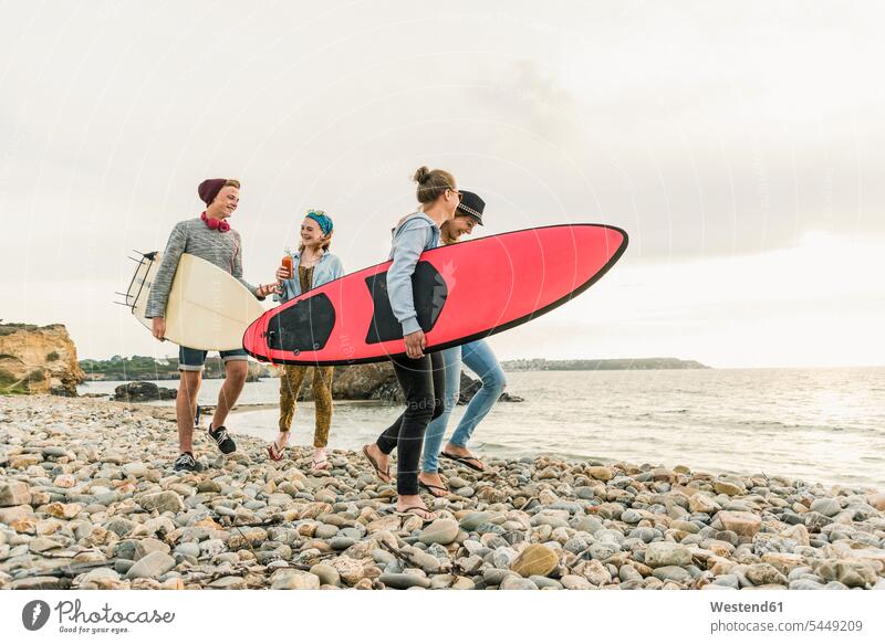 Happy friends with surfboards walking on stony beach surfer surfers happiness happy beaches surfing surf ride surf riding Surfboarding water sports Water Sport