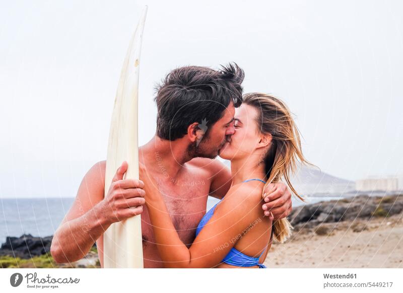 Young couple with surfboard kissing on the beach surfboards kisses Love loving twosomes partnership couples surfing surf ride surf riding Surfboarding beaches