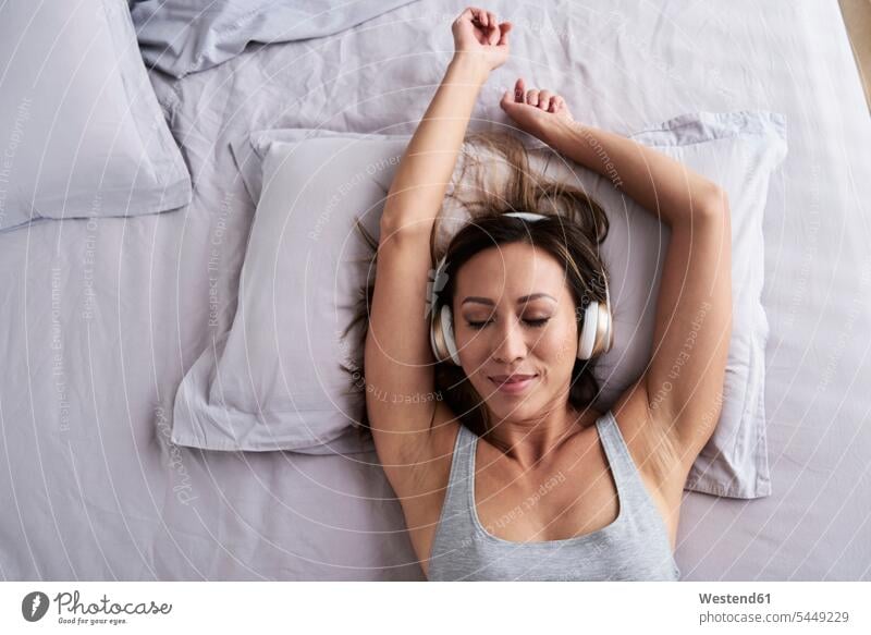 Relaxed woman listening to music in bed hearing relaxed relaxation beds females women relaxing Adults grown-ups grownups adult people persons human being humans