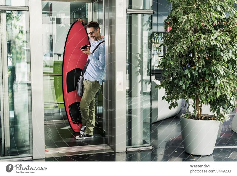 Smiling businessman with surfboard and cell phone in elevator surfboards Businessman Business man Businessmen Business men mobile phone mobiles mobile phones