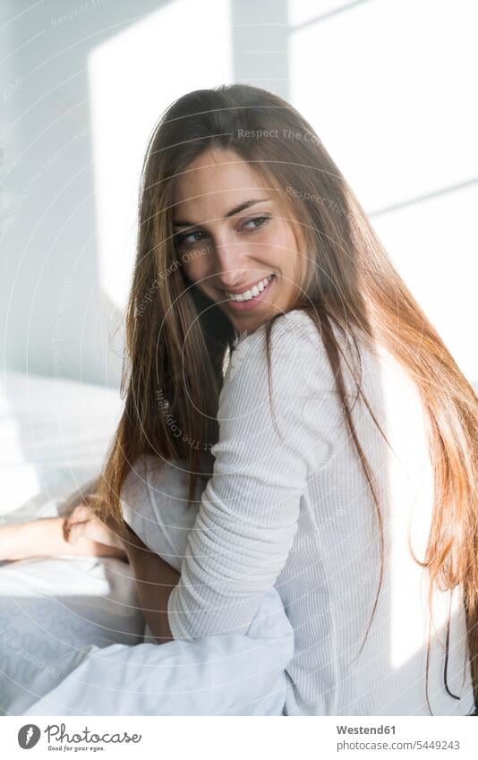 Smiling young woman sitting on bed females women smiling smile beds Adults grown-ups grownups adult people persons human being humans human beings home at home