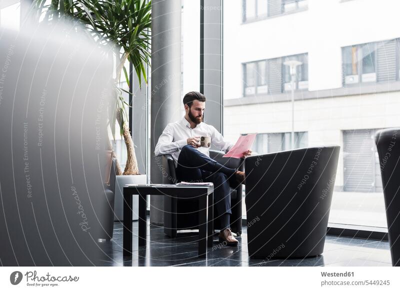 Businessman sitting in lobby, drinking coffee, reading documents caucasian caucasian ethnicity caucasian appearance european working At Work armchair Arm Chairs