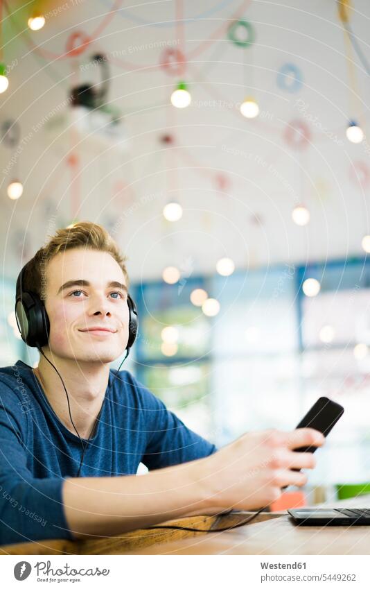 Portrait of relaxed young man listening music with headphones and smartphone in a coffee shop headset portrait portraits smiling smile men males Smartphone