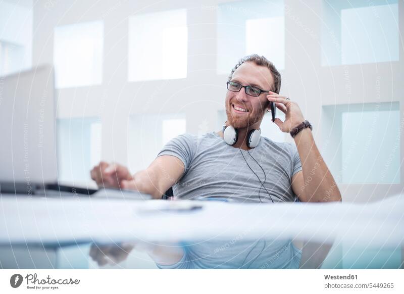 Young man with headphones around his neck talking on the phone cool attitude composed coolness laid-back call telephoning On The Telephone calling Office