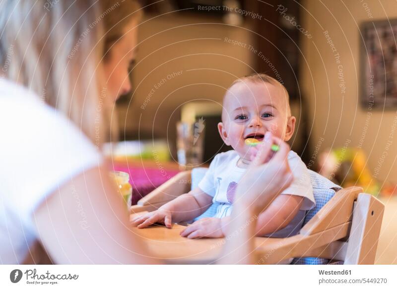 Mother feeding her baby son at home sons manchild manchildren mother mommy mothers mummy mama eating infants nurselings babies family families people persons