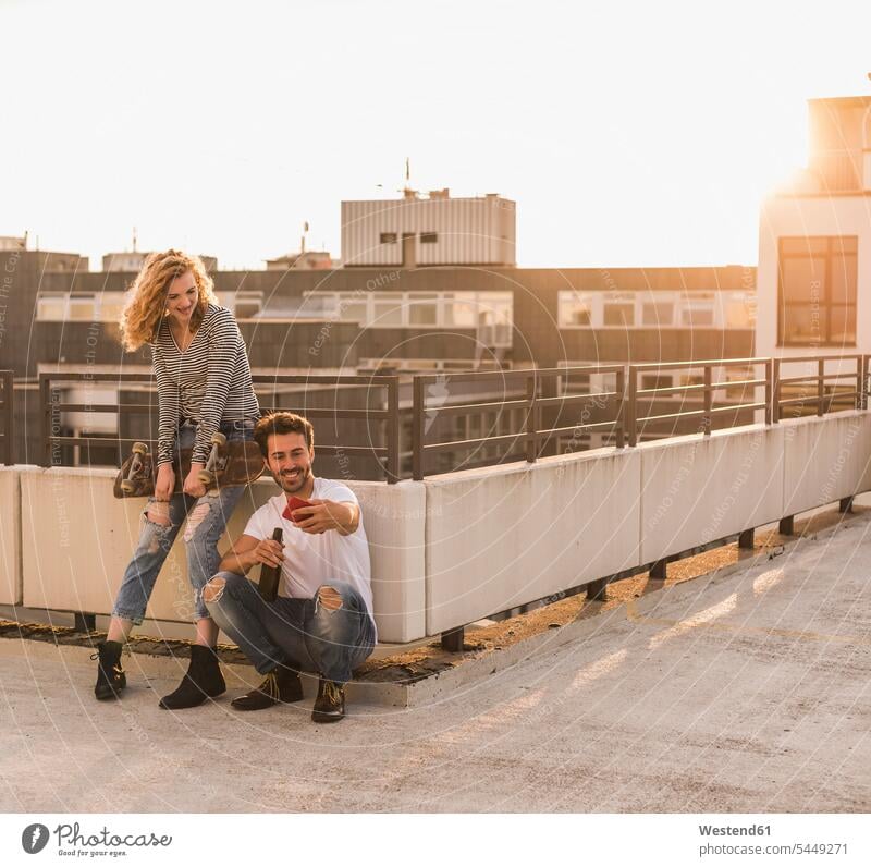 Young couple relaxing on roof terrace at sunset taking selfie with cell phone relaxation relaxed Smartphone iPhone Smartphones Selfie Selfies deck rooftop