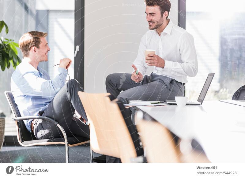 Two smiling colleagues working on project in office together smile talking speaking Businessman Business man Businessmen Business men offices office room