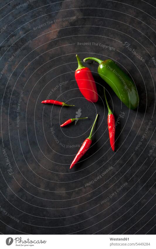 Five red organic chili peppers and a green one on dark ground variation gleaming various different organic edibles arrangement grouping firm sort sorts divers